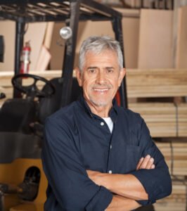 confident senior carpenter with arms crossed standing in workshop